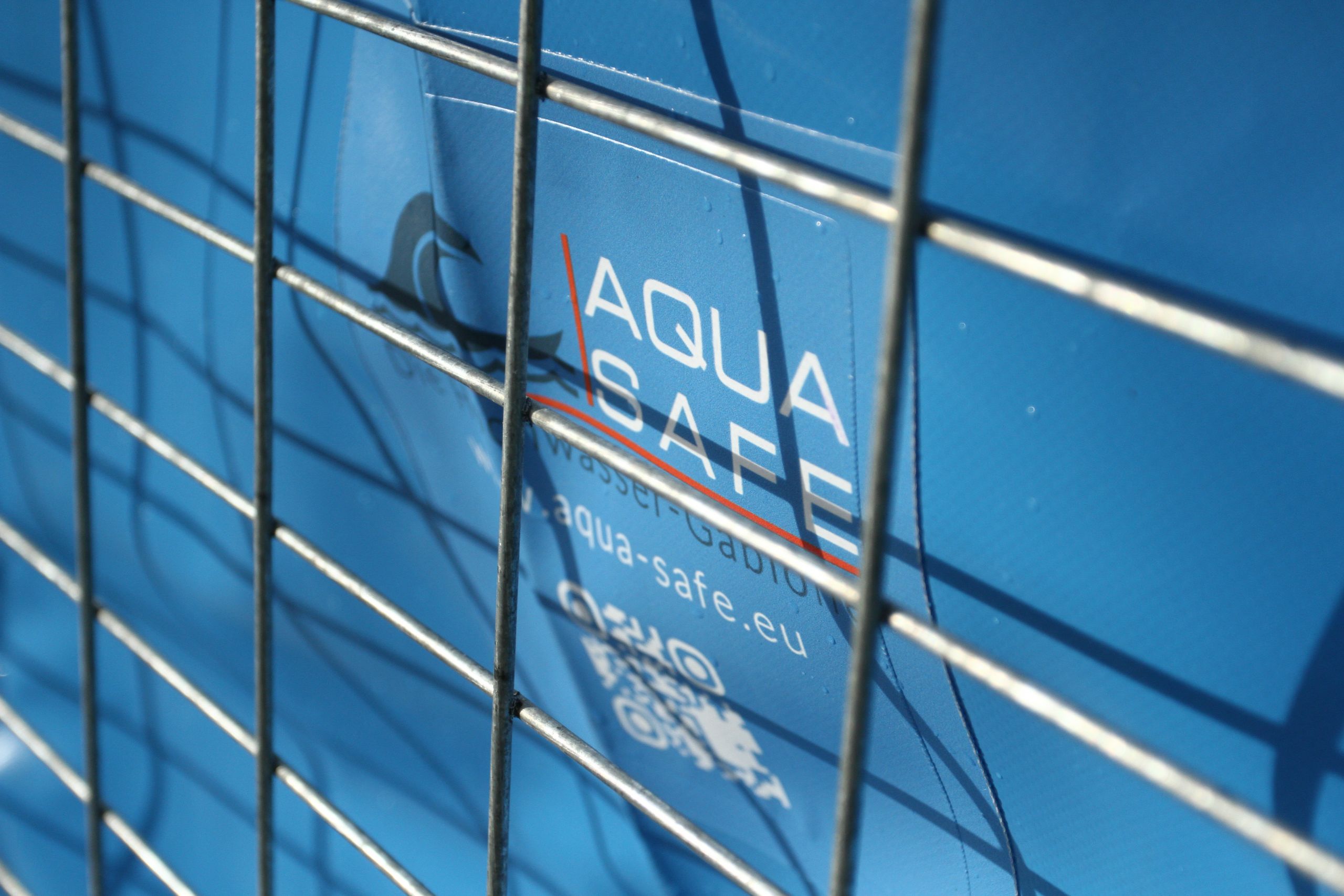 Nahaufnahme des Aqua-Safe-Logos auf einem blauen Wassertank mit stabilem Metallgitterrahmen.