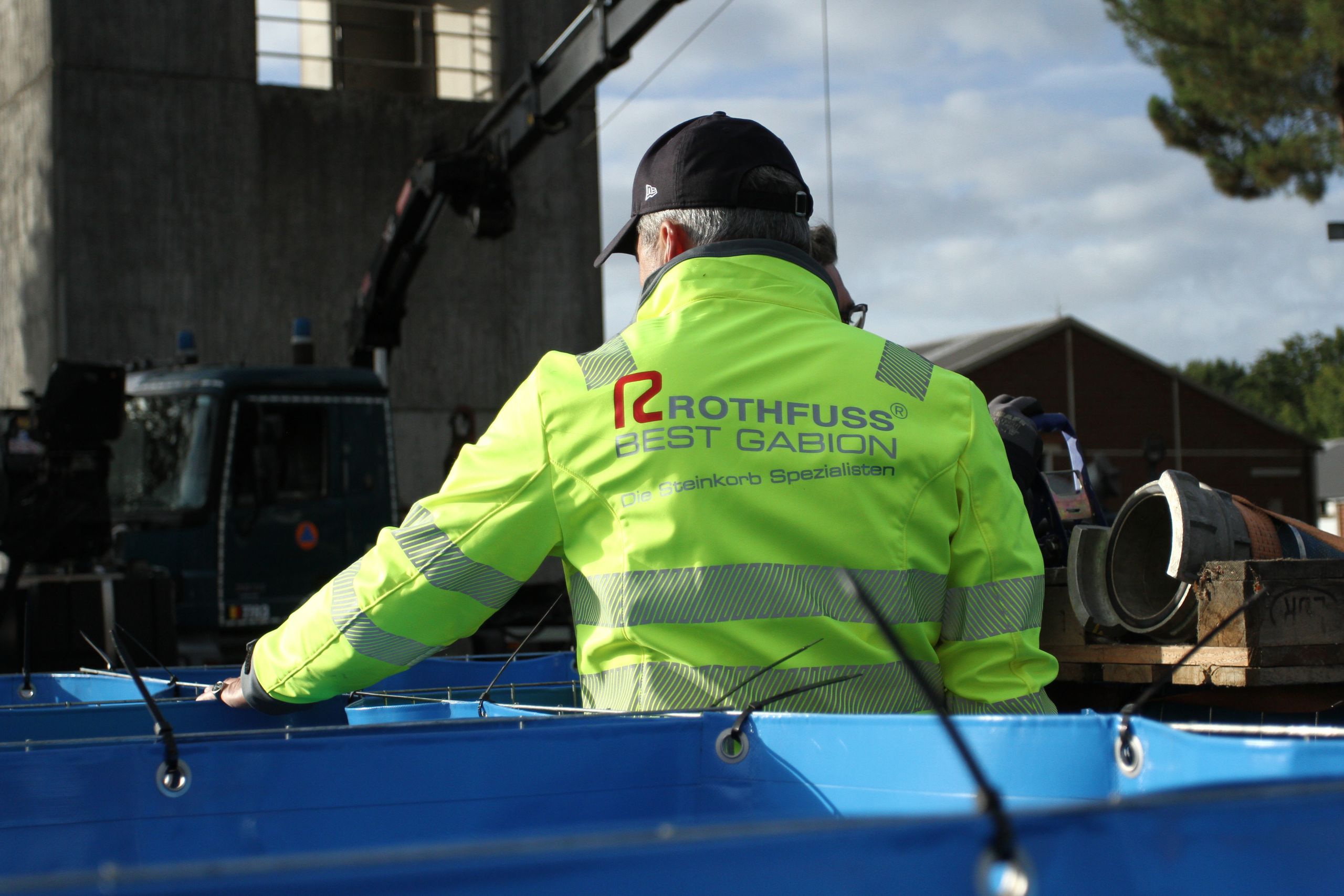 Mitarbeiter von Rothfuss Best Gabion in Warnjacke beim Aufbau blauer Wassertanks auf einer Baustelle.