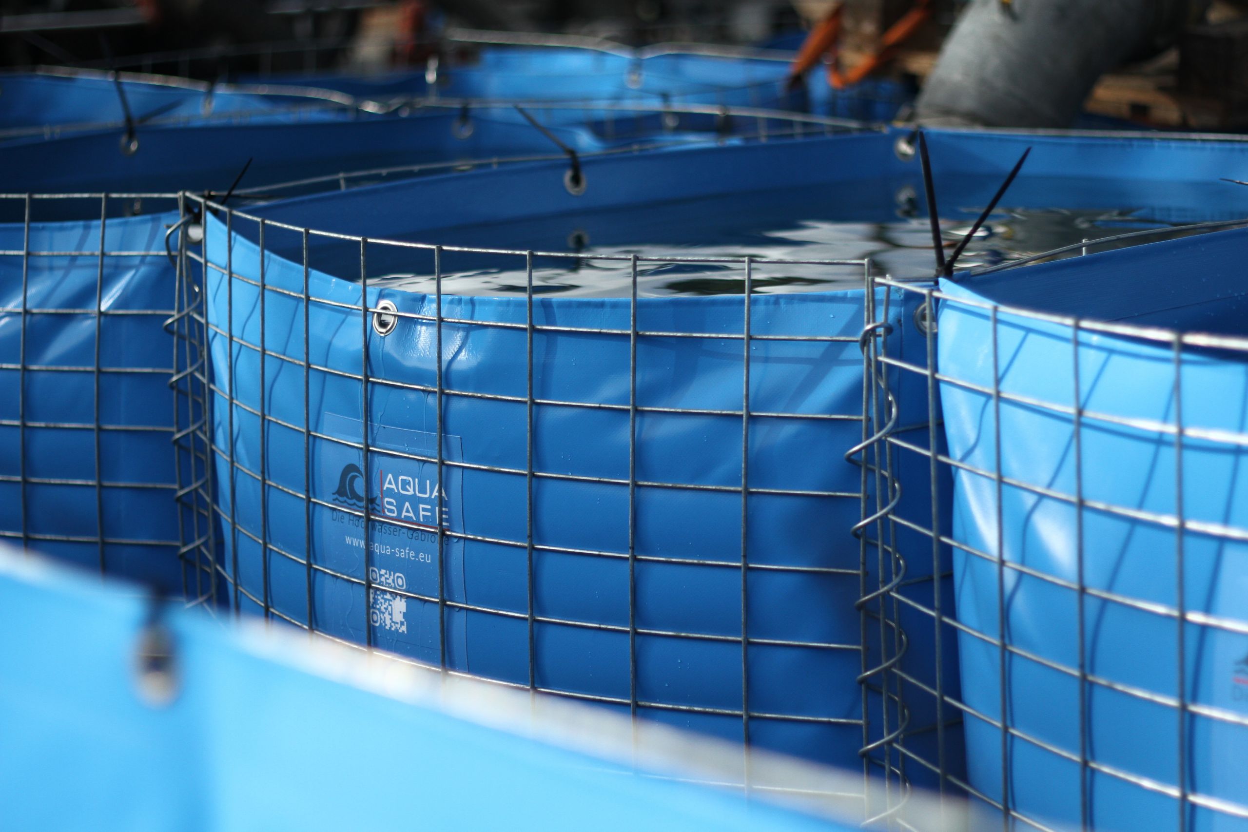 Blaue flexible Wassertanks mit Metallgitterrahmen von Aqua-Safe zur sicheren Wasserspeicherung auf Baustellen oder in Industrieanlagen.